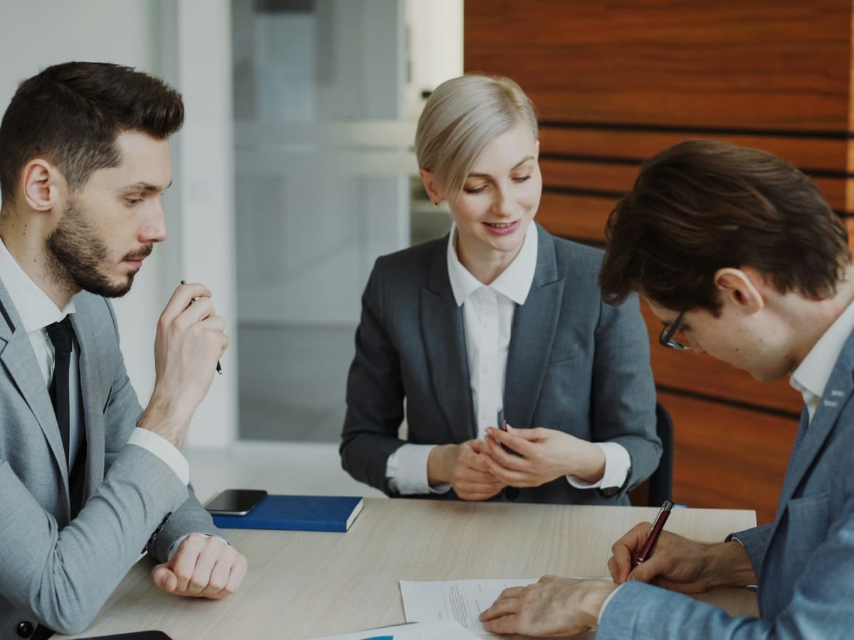 Three professionals reviewing and signing documents in a meeting room